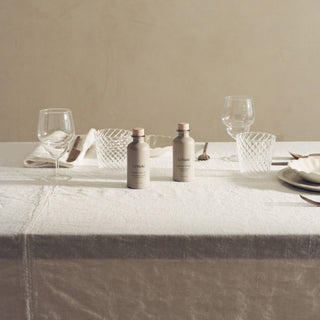 Dining table setting with bottles, glasses, and cutlery on a neutral background
