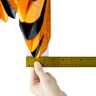 Hand holding a measuring tape next to a colorful kite on a white background