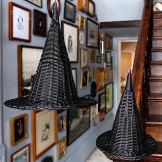 Black woven hat sculptures on wooden stands against a wall with framed pictures