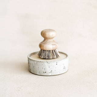 Ceramic dish scrubber with wooden handle on a light beige background