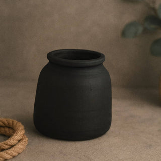 Black ceramic vase on a brown surface with stones and rope