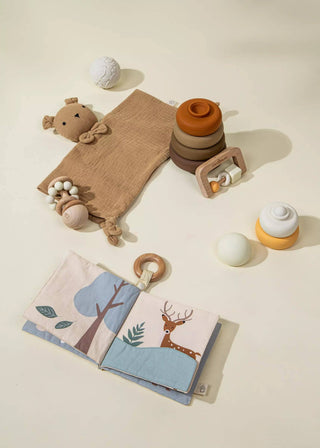 Collection of baby toys including a soft book, rattle, and teether on a neutral background