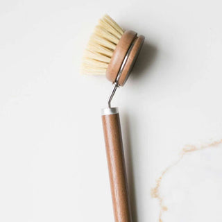 Dish brush with wooden handle and beige bristles on a light marble background
