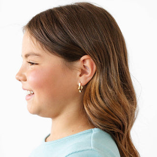 Side profile of a young girl with a ponytail wearing gold earrings on a white background
