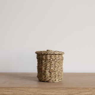Woven basket with a lid on a wooden surface against a plain background