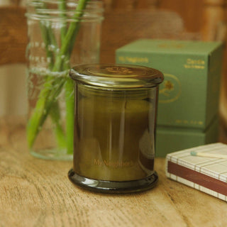 Green candle in a glass jar on a wooden surface with a blurred background