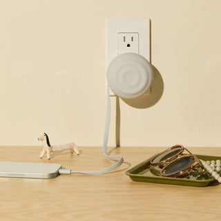 White cylindrical device plugged into a wall socket on a wooden surface with a small dog figurine and decorative items.
