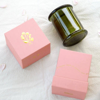 Green candle in a pink box on a white surface with scattered petals