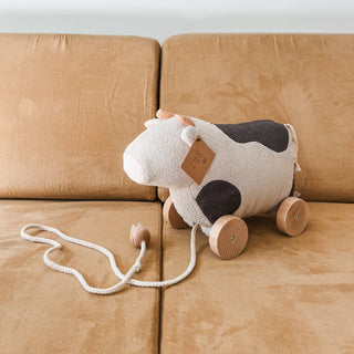 Cow-shaped pull toy with wooden wheels on a beige couch