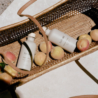 Two white bottles with black text on a woven basket with fruits on a light surface