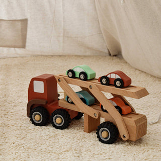 Wooden toy truck with a carrier rack holding multiple small cars on a textured surface.