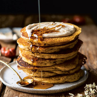 Stack of pancakes with syrup and whipped cream on a plate, served on a wooden table.