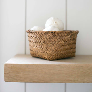 Woven basket with white balls on a wooden shelf against a white paneled wall