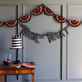 Halloween-themed decor with 'Trick or Treat' banner, striped cake, and candy on a wooden table against a gray wall.
