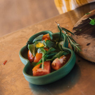 Green dish with sliced tomatoes and herbs on a wooden surface
