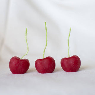 Three candles in the shape of cherries lined up on a white background