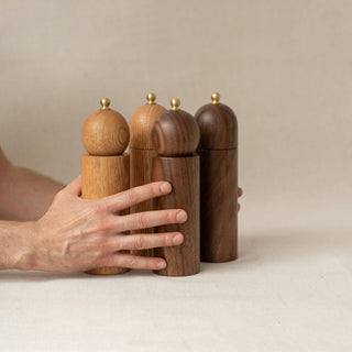 Set of wooden pepper mills on a neutral background with a hand reaching for one.