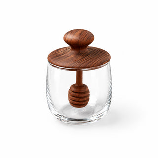 Glass container with wooden lid and honey dipper on a yellow background