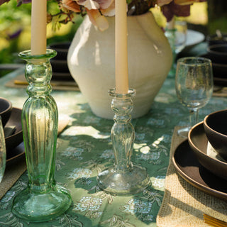 Decorative table setting with flowers, candles, and green candlestick holders on a patterned tablecloth.