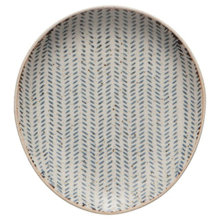 A round ceramic plate with a textured, speckled beige exterior and a white interior decorated with a repeating blue-gray herringbone pattern.