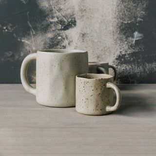 Two ceramic mugs on a wooden surface with a textured wall background