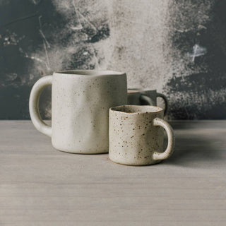 Two ceramic mugs on a wooden surface with a textured wall background
