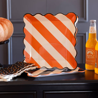 Decorative plate with orange and white stripes on a dark surface with bottles and a pumpkin.