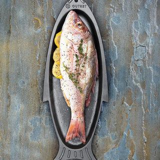 Prepared fish on a metal tray with herbs and lemon slices against a textured stone background