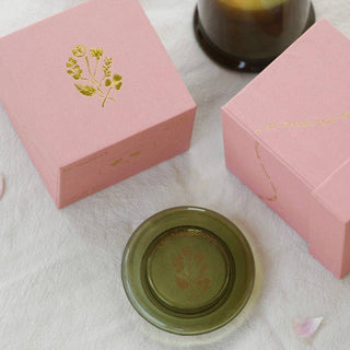Pink boxes with gold designs and a candle on a light surface