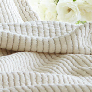 Close-up of a textured white blanket with flowers in the background