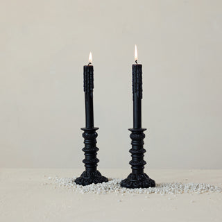 Two black candlesticks with lit candles on a light gray background