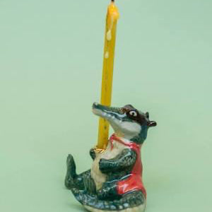 Decorative alligator candle holder with a lit yellow candle on a light green background